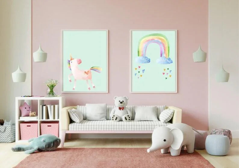 Two white-framed art prints of a unicorn and a rainbow on a pink wall in a child's room above a small couch.