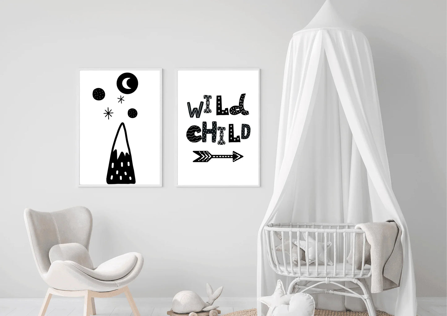 Mockup of two black and white minimalist nursery art posters hanging above a crib. The prints feature a mountain, moon, and stars, and the text "WILD CHILD" with an arrow. The room has Scandinavian decor with a white canopy, a light gray chair, and a neutral, gender-neutral color palette.