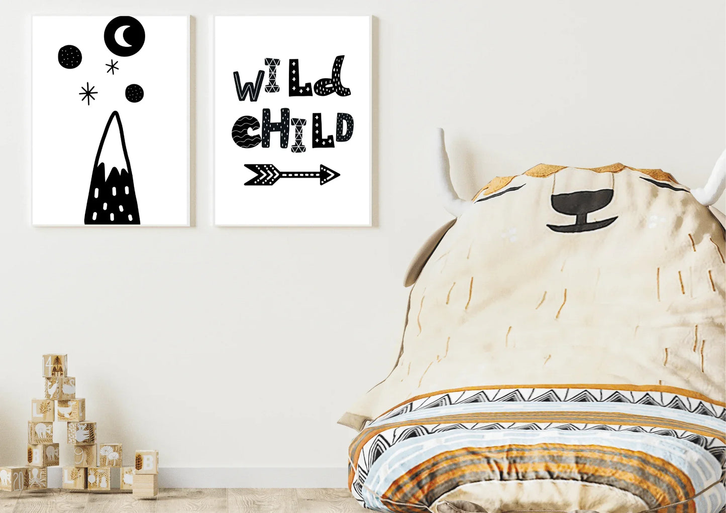 lack and white nursery wall art set featuring a mountain with a moon and stars, and a print with the text "WILD CHILD" and an arrow, hanging above wooden blocks and a large, bean bag chair.