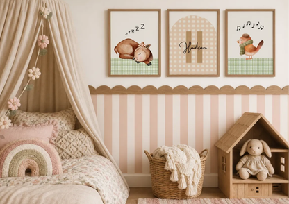 A styled children's bedroom corner with three framed nursery wall prints above a bed. The prints show a sleeping bunny with 'zzz', the name 'Hudson' in script, and a bird with musical notes.