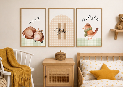 Three framed nursery wall art prints hang above a wooden crib in a styled children's room. The prints feature watercolor illustrations: a sleeping deer with 'zzz' text, a gingham arch with the name 'Hedwig', and a bird with musical notes.