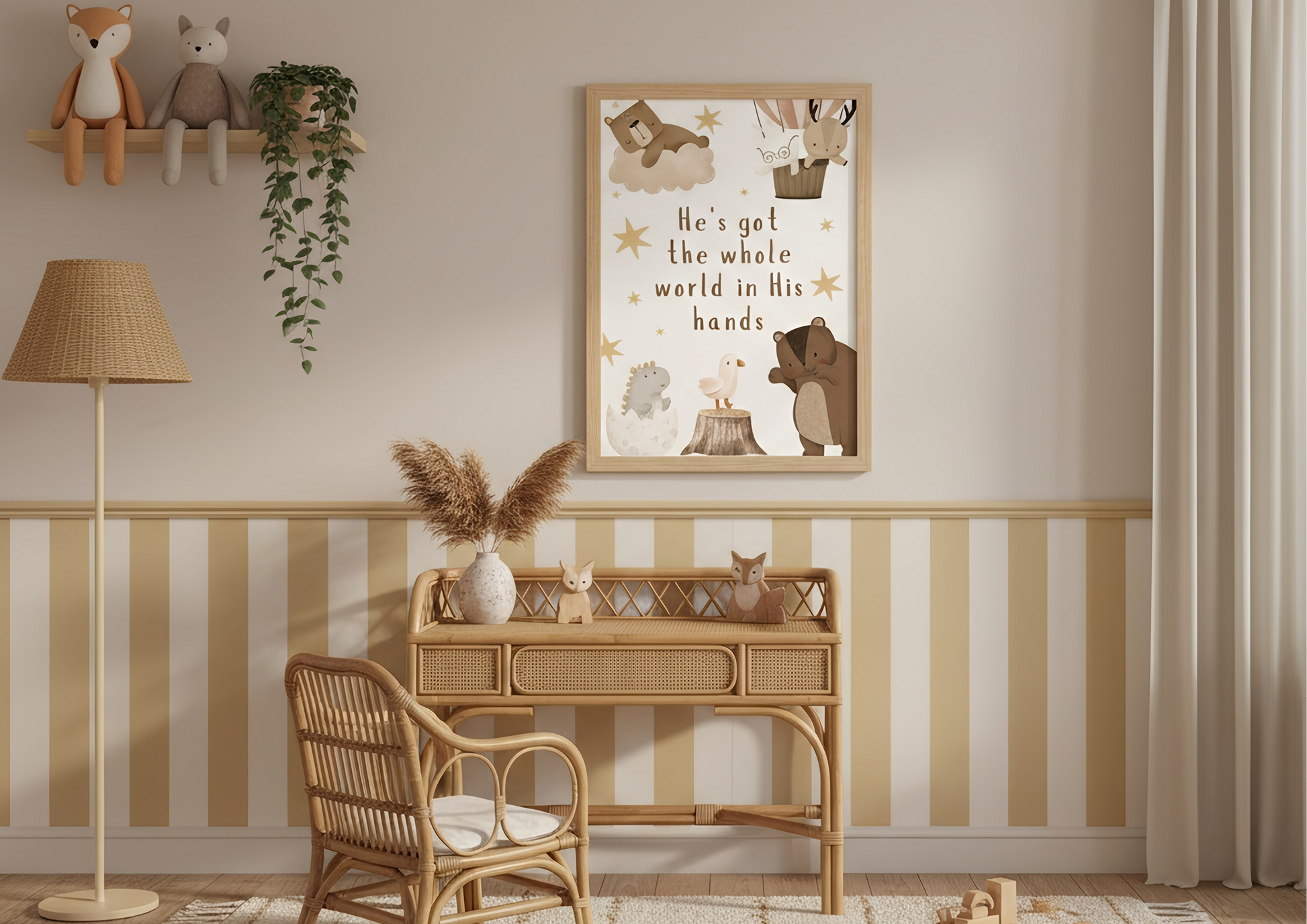 
A cozy nursery or child's room corner featuring a rattan desk and chair. Hanging above the desk is a framed Christian wall art print with the lyric "He's got the whole world in His hands" surrounded by cute woodland animals in a soft, neutral color palette. The lower half of the wall is decorated with wide vertical stripes in cream and light yellow.