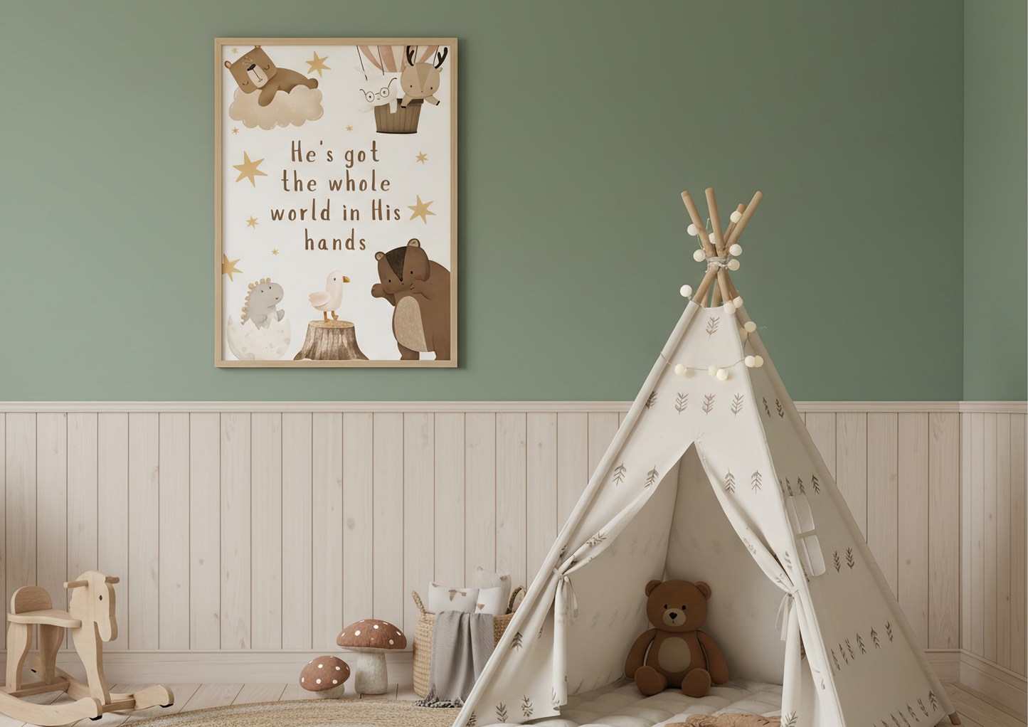A close-up of a child's room featuring a framed Christian woodland art print with the phrase "He's got the whole world in His hands" and watercolor forest animals, hanging against a sage green wall. Below, a white teepee with string lights sits on the floor, next to light wood wainscoting and a wooden rocking horse.