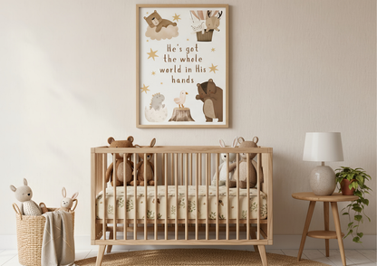 A charming nursery scene featuring a light wood crib with neutral bedding and several stuffed animals. Hanging above the crib against a light beige wall is a framed Christian wall art print with the lyric "He's got the whole world in His hands" and cute watercolor woodland animals. A small wooden side table with a lamp and plant is visible on the right.