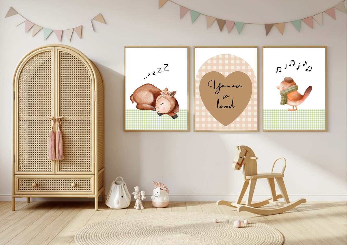 Three framed nursery wall art prints displayed on a light gray wall in a styled children's room. The prints feature cute illustrations: a sleeping cow with 'zzz' text, a heart with 'You are so loved' in the center, and a singing bird with musical notes on the right.