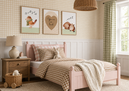 A styled children's bedroom featuring a light pink wooden bed with a brown and beige gingham checkered comforter and matching pillow. Above the bed, three framed animal illustrations hang on a cream and beige gingham wall with white wainscoting.