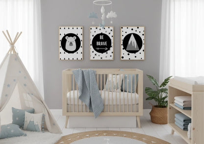 Three monochrome nursery prints featuring a bear, "Be Brave" text, and a mountain, hanging above a wooden crib in a neutral-toned nursery with a teepee and plants.