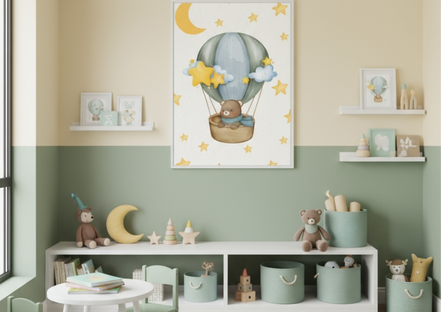 A vertical framed nursery wall art print hanging on a wall painted in two colors: light yellow on the top half and muted sage green on the bottom half. The artwork features a cute teddy bear wrapped in a blue scarf, riding in a wicker basket attached to a blue and green hot air balloon. The scene is surrounded by yellow stars and a crescent moon on a cream background. The wall features white floating shelves on either side of the main artwork, holding smaller framed prints and wooden toys. Below the print i