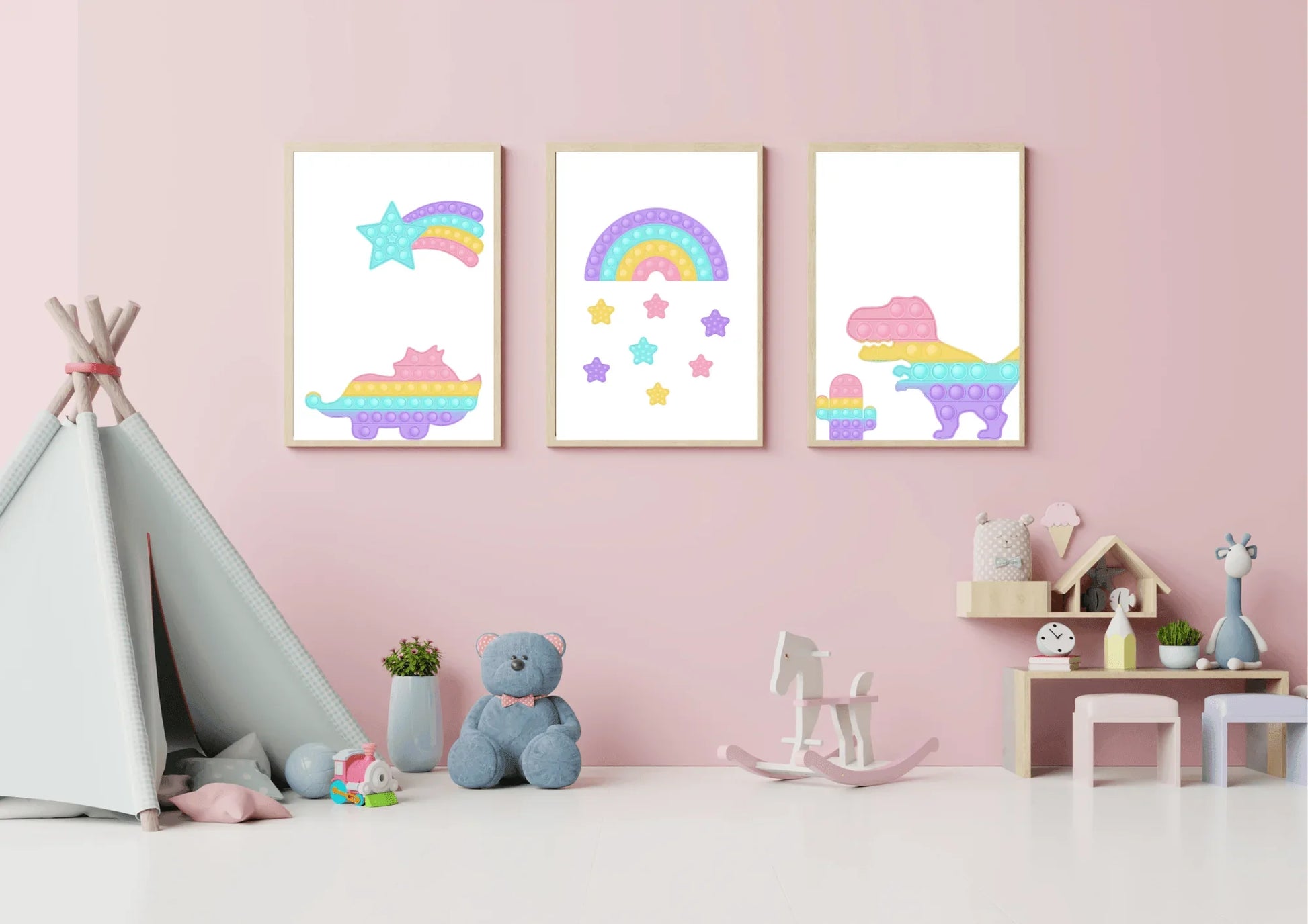 A three-piece nursery print set, featuring pop-it style dinosaurs, a rainbow, and a shooting star, hanging on a pink wall above a teddy bear and a rocking horse.