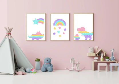 A three-piece nursery print set, featuring pop-it style dinosaurs, a rainbow, and a shooting star, hanging on a pink wall above a teddy bear and a rocking horse.