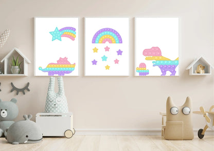 A three-piece nursery print set, featuring pop-it style dinosaurs, a rainbow, and a shooting star, hanging on a light beige wall above a variety of stuffed animals and children's toys.