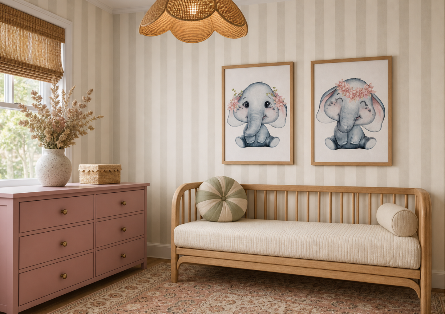 A styled nursery or children's room corner featuring two framed watercolor prints of baby elephants on a striped wall above a light wood daybed with cream bedding. To the left is a dusty pink wooden dresser with brass knobs and a woven rattan pendant light overhead.