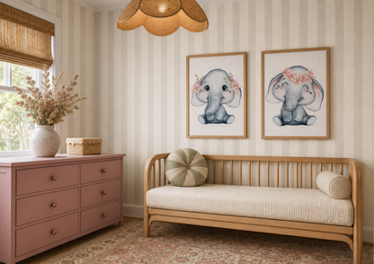 A styled nursery or children's room corner featuring two framed watercolor prints of baby elephants on a striped wall above a light wood daybed with cream bedding. To the left is a dusty pink wooden dresser with brass knobs and a woven rattan pendant light overhead.